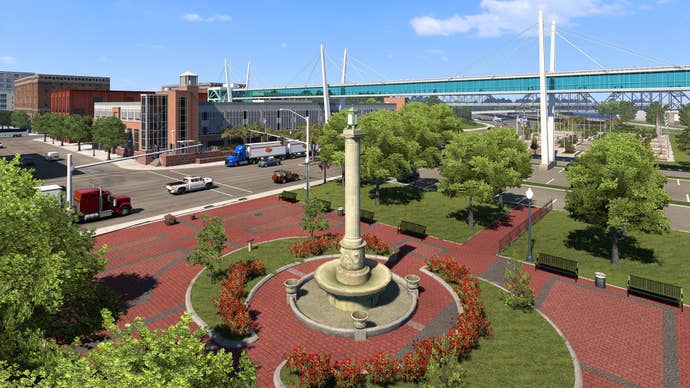 A screenshot of American Truck Simulator’s Iowa expansion showing a column-like fountain in a city plaza surrounded by trees.