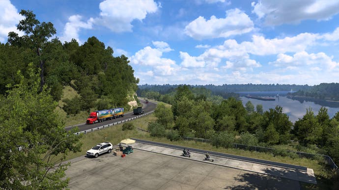 A screenshot from American Truck Simulator's Iowa expansion showing a truck passing a carpark overlooking a vast picturesque lake.