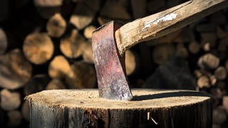 A photograph of a rusted hatchet axe buried in a tree stump. In the background are piles of chopped wood. Someone has been busy.