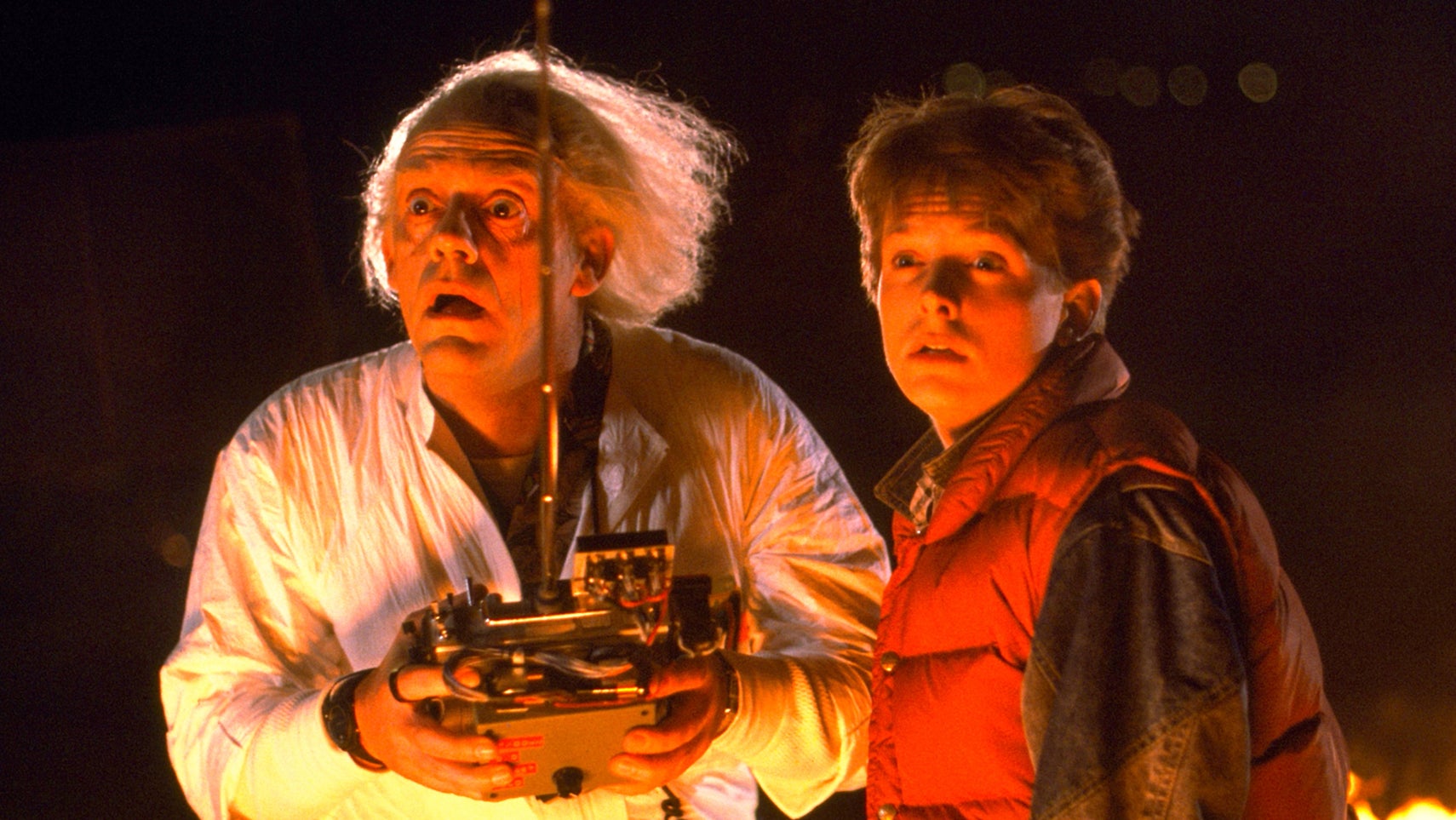 Doc Brown looks surprised while holding a remote control device, with Marty McFly looking surprised next to him in Back to the Future. - 1