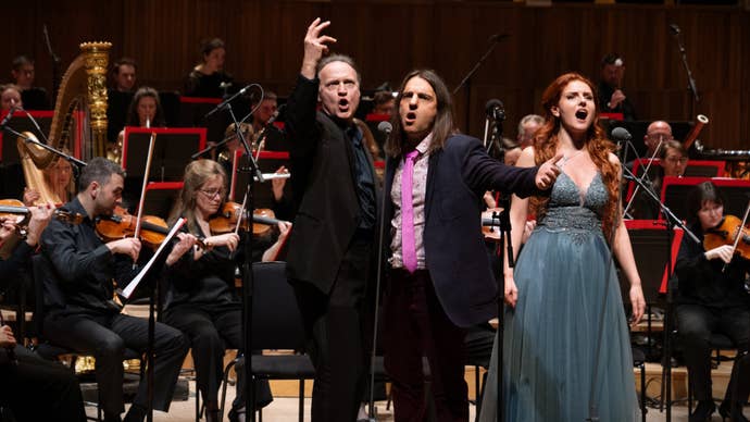 A photo of an orchestral performance of Baldur’s Gate 3 music, although it’s slightly unusual in that you have two men and a woman at the front of the stage, singing. The woman is one of the vocalists from the Baldur’s Gate 3 soundtrack. The smaller of the men, with long brown hair, is the composer Borislav Slavov, and the taller man, who’s a little older with cropped hair, is the actor Andrew Wincott, who played the character Raphael in the game. They are all belting out Raphael’s Final Act song, mouths open, dramatically gesturing. It’s a powerful image!