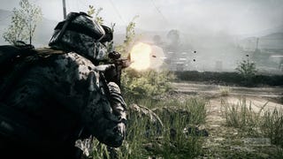 A Battlefield 3 screenshot showing an over-the-shoulder view of a solder firing his weapon while crouching in the grass.