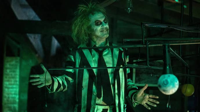 Michael Keaton as Beetlejuice, a man with pale skin, wild unkept hair, and a black and white stripey suit, doing jazz hands.