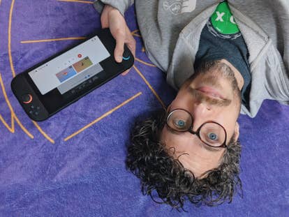 A photograph of Eurogamer writer Bertie, who's lying on a bed holding a Switch 2 console at a very strange angle. Is it a saucy image? Not really. Is it strange? Very much so.