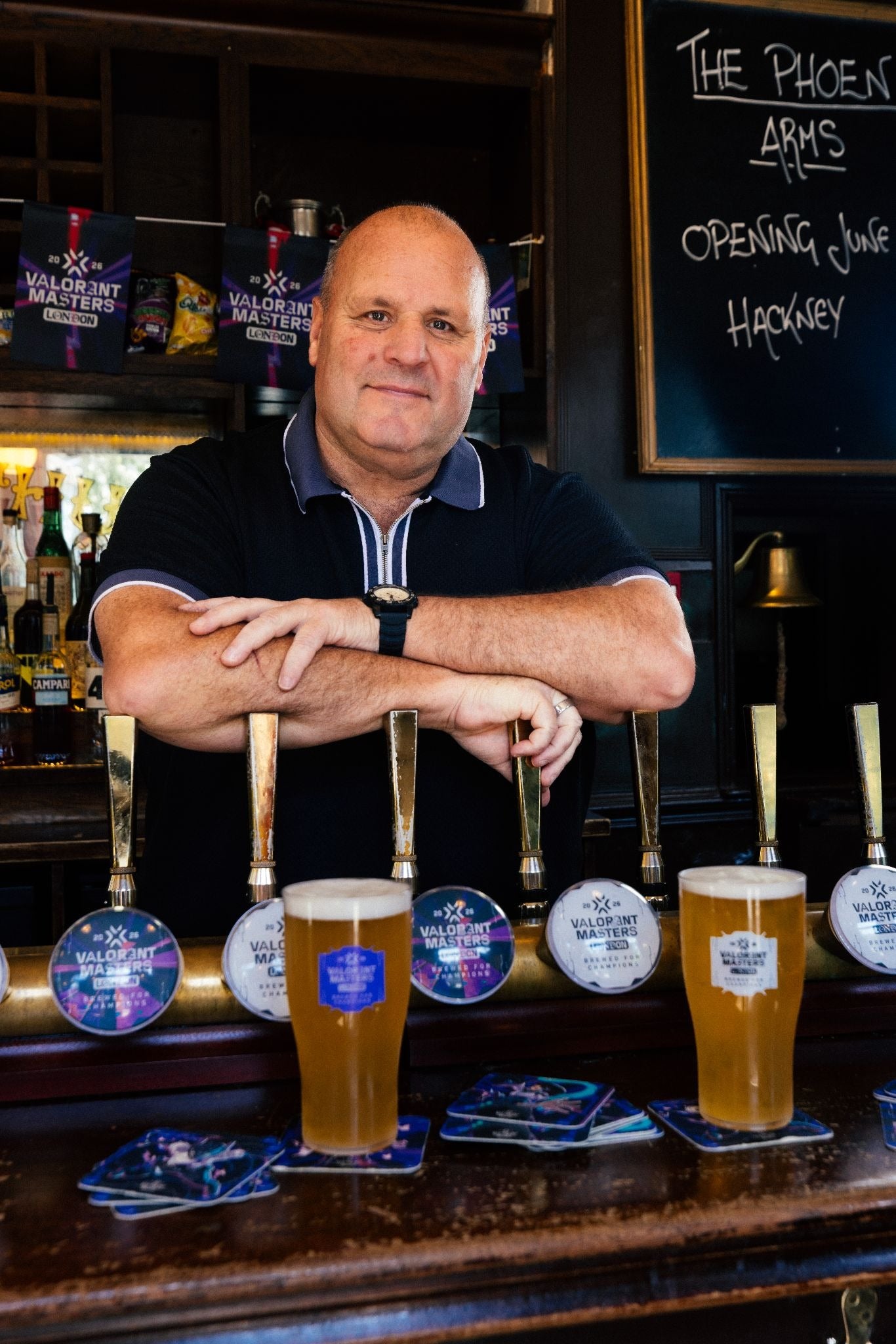 A big white chap with a bald head stands with his arms folded on some beer pump handles in a pub. A couple of lonely pints stand on the bar in front of him. Go ahead, he's almost saying, drink them. If you dare.