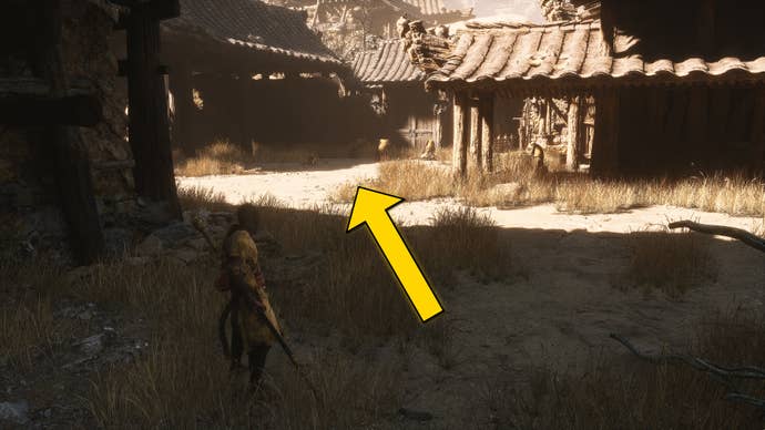 The player in Black Myth: Wukong stands near a building in the Windrest Hamlet in Chapter 2. A yellow arrow points towards an open square outside the building.