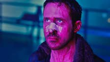 Ryan Gosling in Blade Runner 2049, stood with a bandage across his face, blood streaming down it, bathed in a purple light looking up at something.