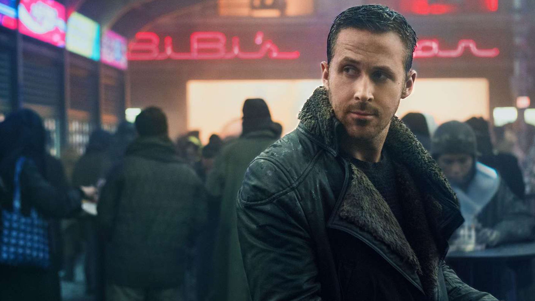 Ryan Gosling in Blade Runner 2049 in a busy futuristic city street looking at something over his shoulder. - 1