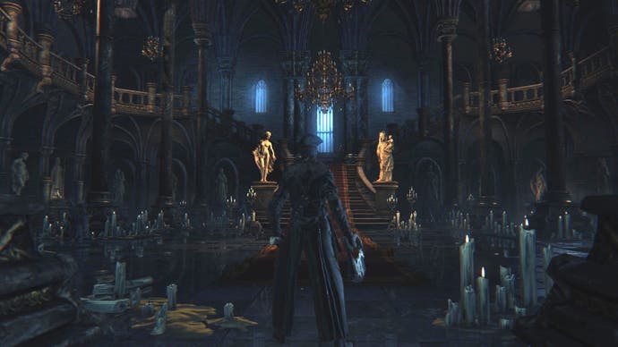 A Bloodborne player character stands inside a large room inside an ornate gothic castle.  The place is littered with candles that aren't giving off much light.