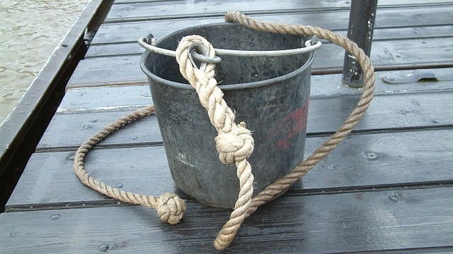 A metal bucket with a rope attached sitting on a wooden platform.