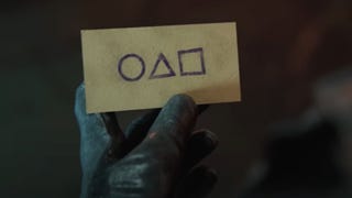 A still from Call of Duty's Squid Game teaser trailer showing a gloved hand holding a small envelop with circle, triangle, and square symbols on the front.