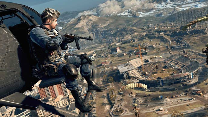 Call Of Duty: Warsone - A view from above the new Verdansk 1984 map. A player rides in a helicopter looking down at the stadium while others parachute in.