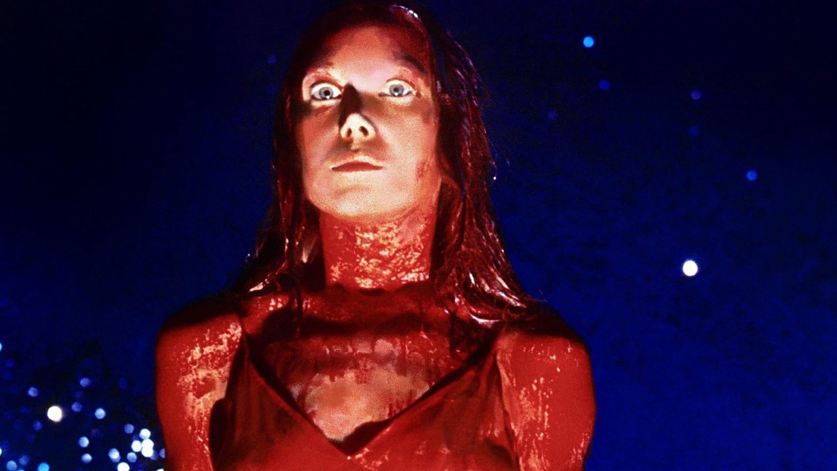 Carrie in the titular movie up on stage, covered in blood, staring intensely at something offscreen. - 1