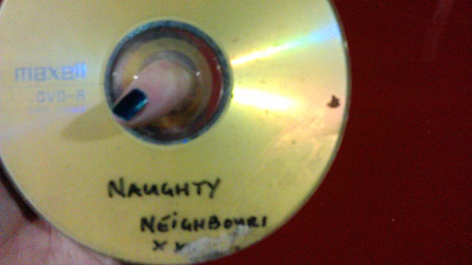 A photograph of a DVD-R with the half-scratched-off label “Naughty Neighbours XXX” written in pen.