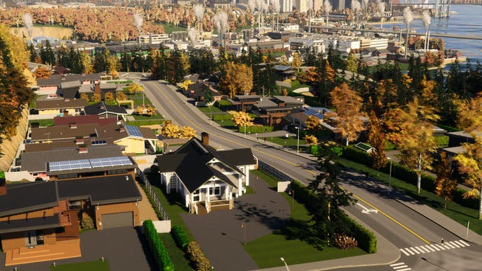 A riverside city on a sunny day built in Cities: Skylines 2. The city is filled with trees lining the roads, and houses along the road have solar panels. In the distance, tall skyscraper builds can be seen. Steam from industrial power plants blows up into the air
