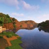 A screenshot of a river in Minecraft, with some trees on either side of the bank and a hill in the distance, taken using Complementary shaders.