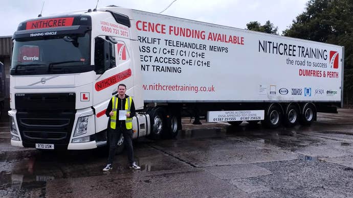 A photograph of a man standing in front of an articulated lorry holding a test certificate up. It’s Craig Wilmott and he’s just passed his test.