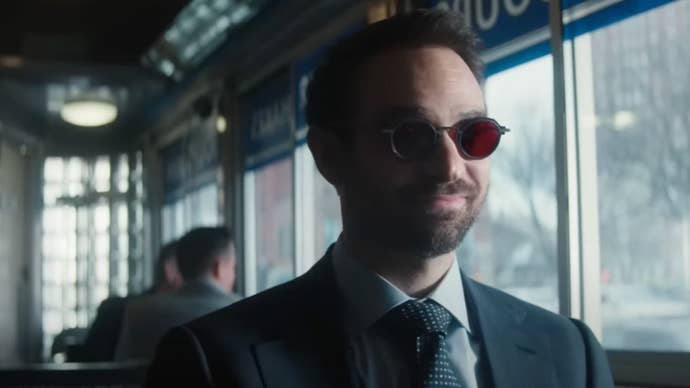 Matt Murdock is sat in a diner wearing his signature red shades while smiling in Daredevil: Born Again.