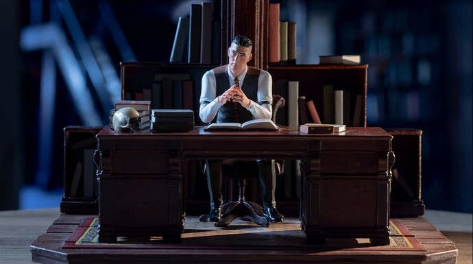 A plastic figurine showing a man in shirt and waistcoat behind a large, dark wooden desk, looking creepy.