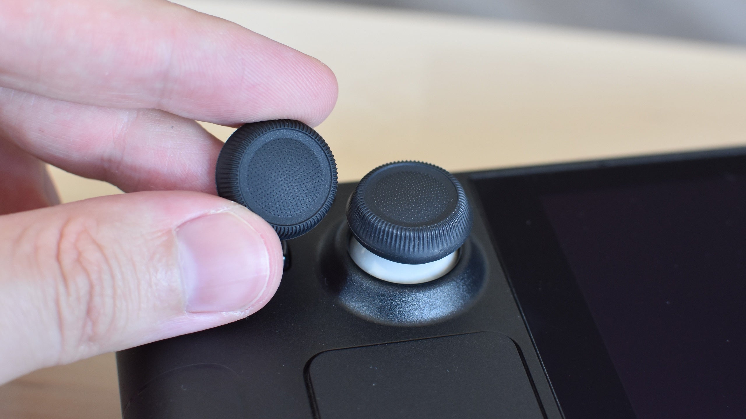 The Dbrand Steam Deck Stick Grips. One is applied to the Steam Deck&rsquo;s left thumbstick, the other is being held next to it.