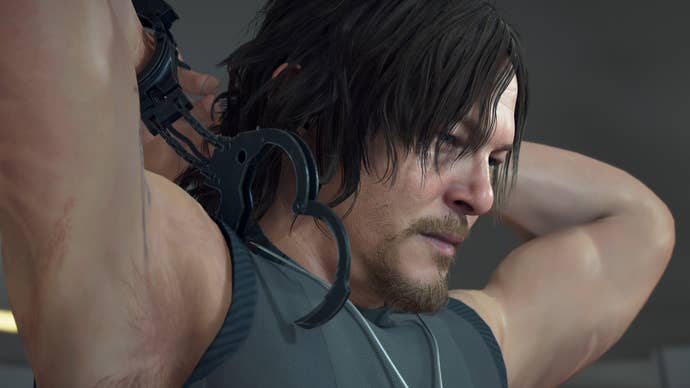 Death Stranding screenshot showing a sweaty Norman Reedus with his hands - one of them handcuffed - around the back of his head.