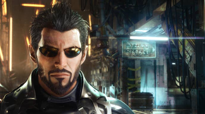 Adam Jensen looks at the camera in his cybernetic sunglasses, as a light beams behind him.