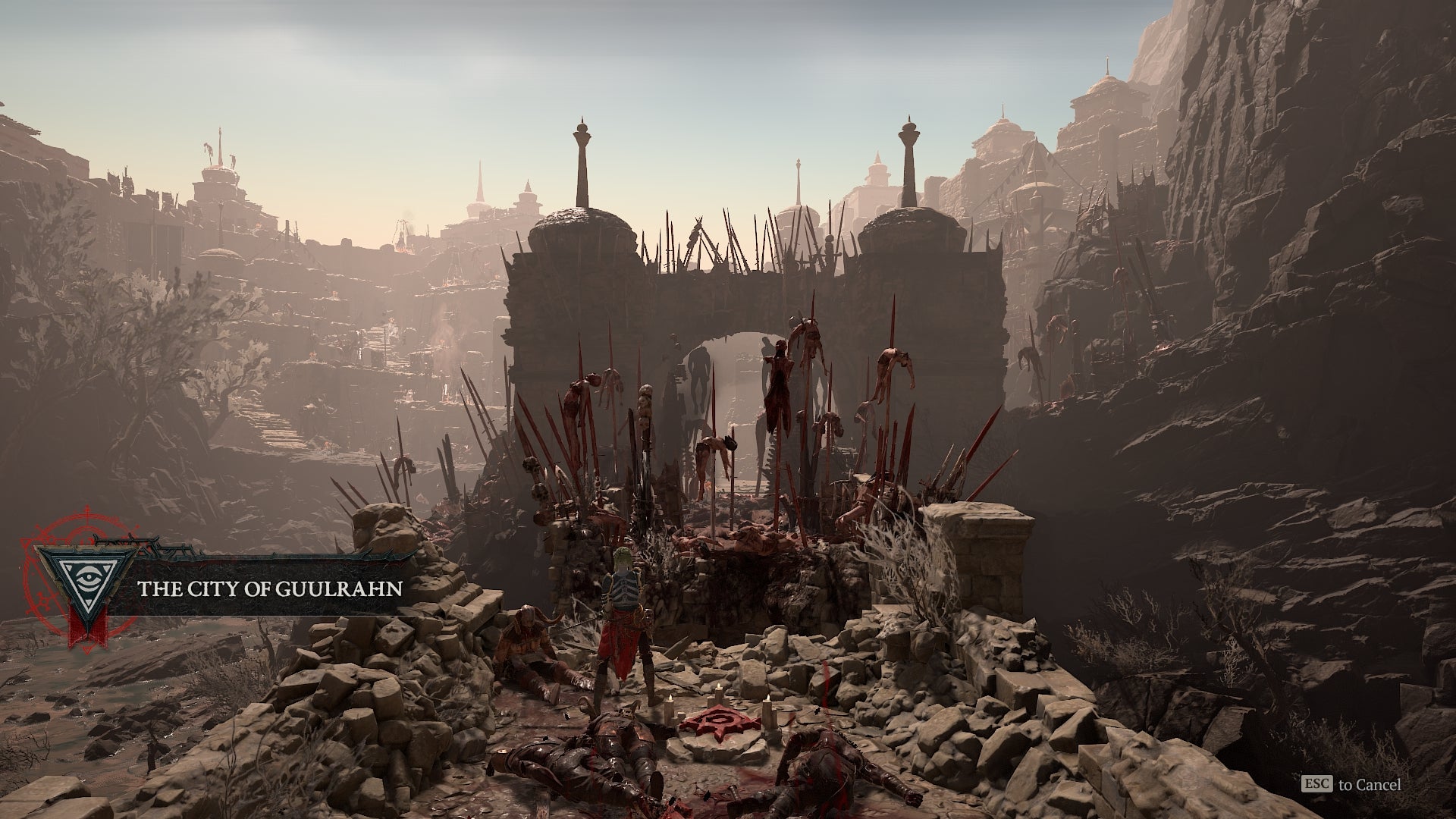 Diablo 4 screenshot showing a grisly view of dozens of bodies on pikes outside a crumbling city&rsquo;s main gate, in a rocky, barren wasteland