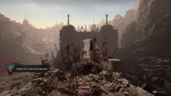 Diablo 4 screenshot showing a grisly view of dozens of bodies on pikes outside a crumbling city's main gate, in a rocky, barren wasteland