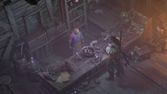 Diablo 4 sigil crafting: A man in furry shoulder pads is standing in front of a counter, speaking with a bald man on the other side of it. The glow of firelight mixes with the eerie purple flames from the shopkeeper’s candles