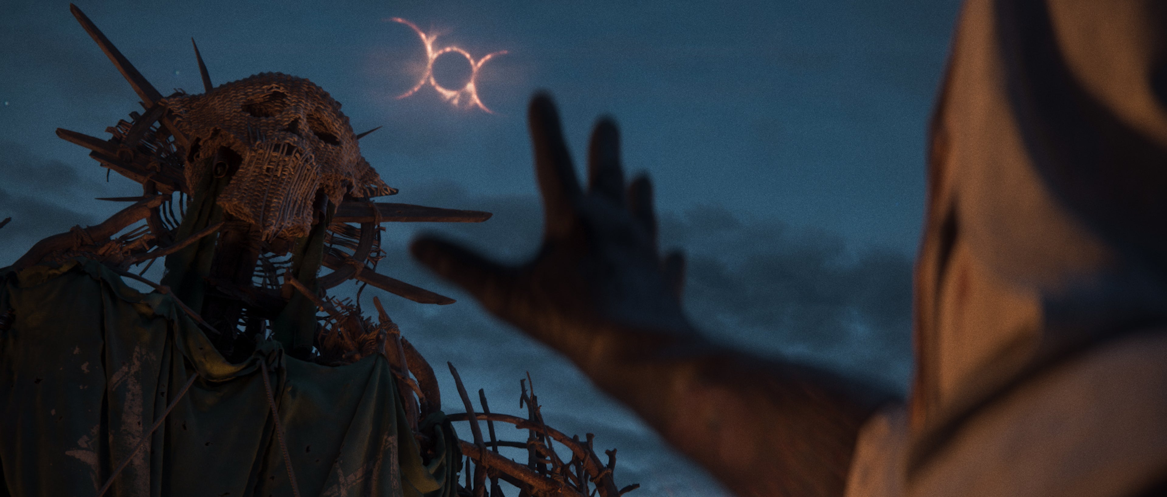 A masked figure gesturing towards a celestial alignment in the dark sky above a huge wickerman in the new Divinity RPG.