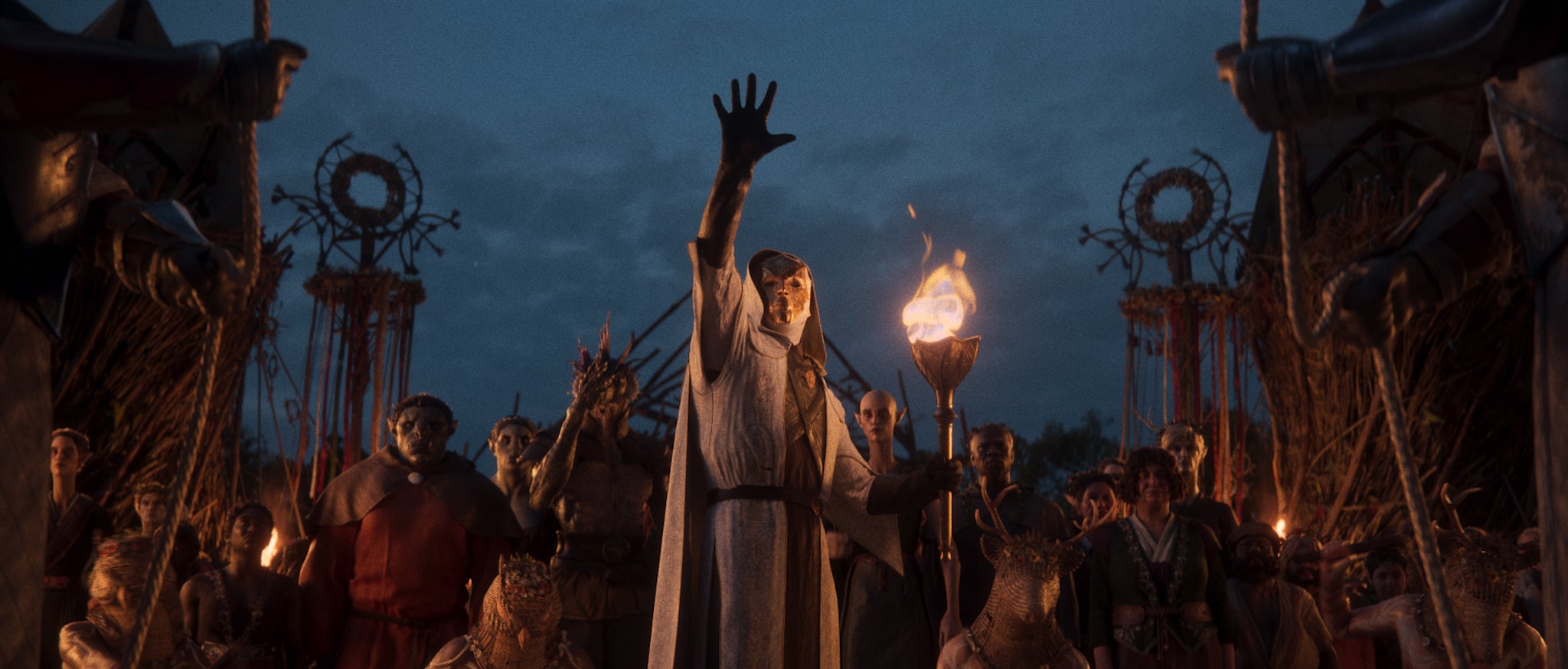 A view of a masked person in robes gesturing upward with a crowd gathered behind him, from a scene in the new Divinity RPG. - 8