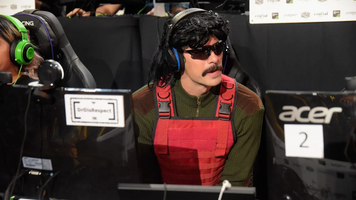 Streamer Dr Disrespect in sunglasses and headphones at a gaming event with a PC in front of him