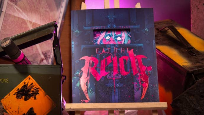 A tabletop role-playing book presented decoratively on a mini-easel. It's Eat the Reich, a game about being vampire commandos and drinking Nazi blood, and it's ridiculously pretty. The front cover is a mixture of dark navy blues contrasted with bright prink game-name lettering. And in a small window, as if it were a prison door - or a metal coffin door, more specifically - you can see the wild eyes of a vampire trapped within.