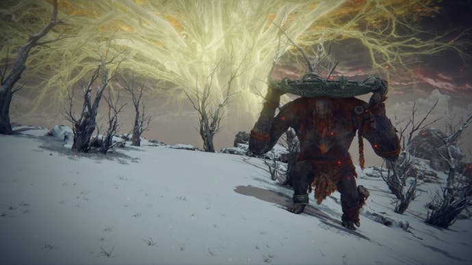 The Fire Giant in Elden Ring hoists his shield above his head and looks towards the camera in the Mountaintops Of The Giants.