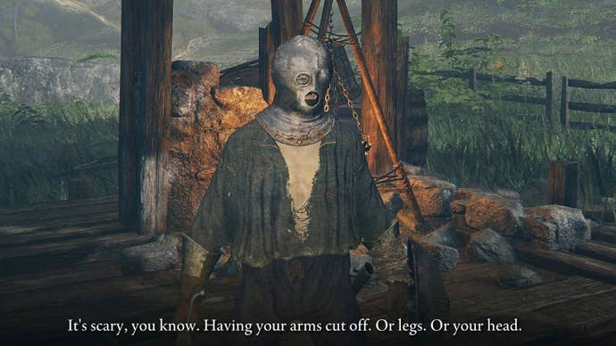 The player character in Elden Ring stands, dressed in rags and wearing an iron mask on their head, stands in a ruined house. An NPC, off screen, has said “It’s scary you know. Having your arms cut off. Or legs. Or your head."