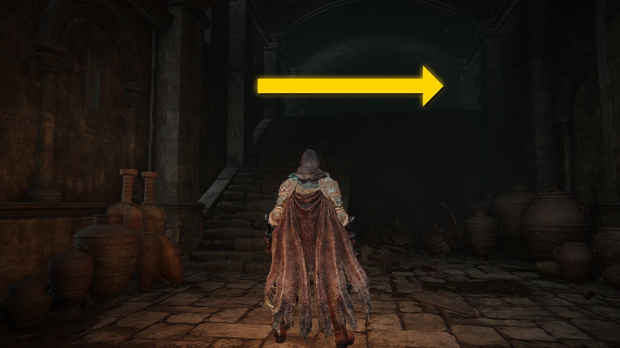 The player in Elden Ring: Shadow Of The Erdtree stands in a dimly lit room at the bottom of a flight of stairs in the Scorched Ruins. - 8