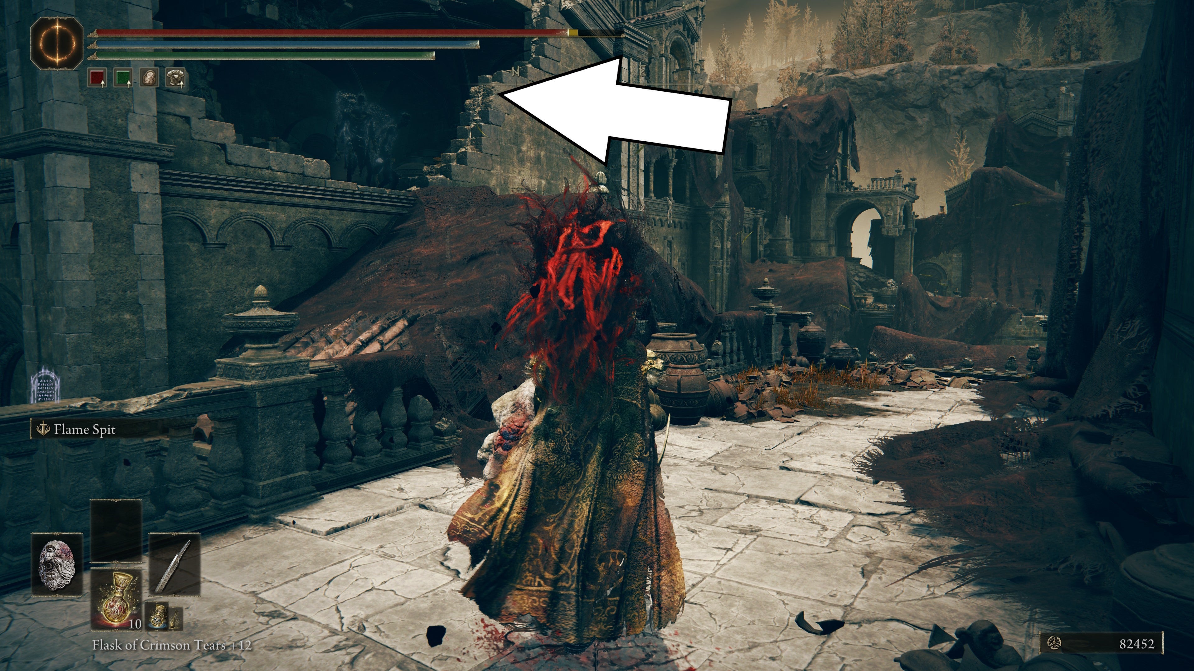 A white arrow points toward an opening on the roof of a ruined building in the Scorched Ruins of Shadow of the Erdtree, showing the way to the Blade of Mercy Talisman