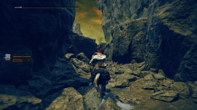 A warrior rides their horse down a dry riverbed as they travel toward the east side of the Shadow Keep in Elden Ring Shadow of the Erdtree.