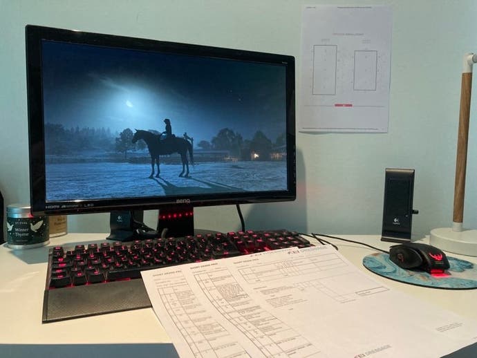A desktop computer with Red Dead Online on the screen, and some papers on the desk and on the wall around it.