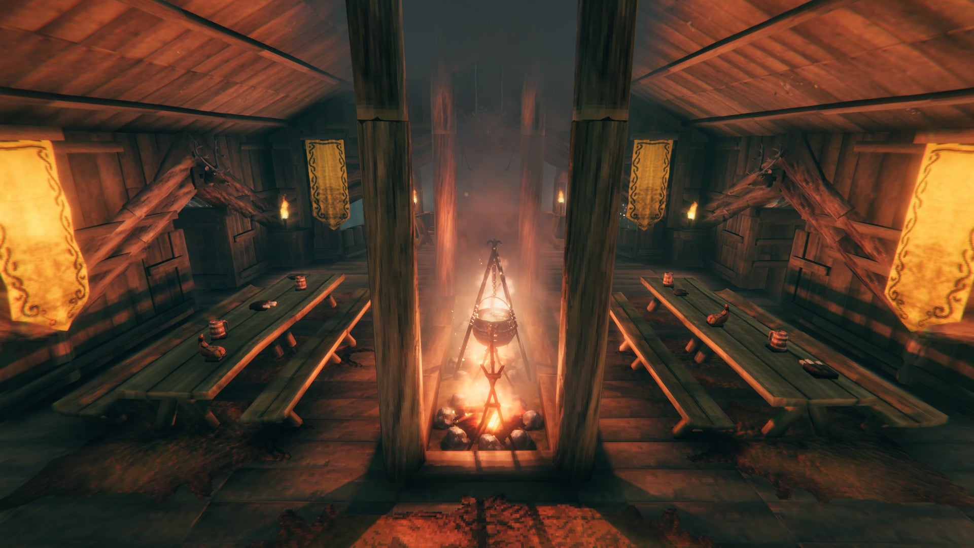 The inside of a Viking log house. There&rsquo;s a fire pit glowing in the middle, illuminating the room, and benches on either side of it.