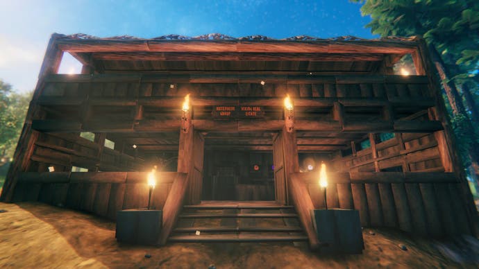 The imposing entrance of a large, multi-story log cabin. Some torches burn at the top of a small flight of stairs. It's the headquarters of Emma's Valheim real estate Hutenheim Group.