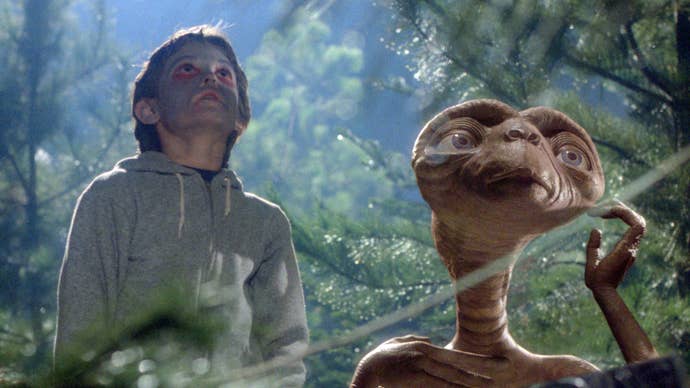 Elliot, a young boy with his face painted, and E.T. a raisin-looking alien, are staring at something in the woods.