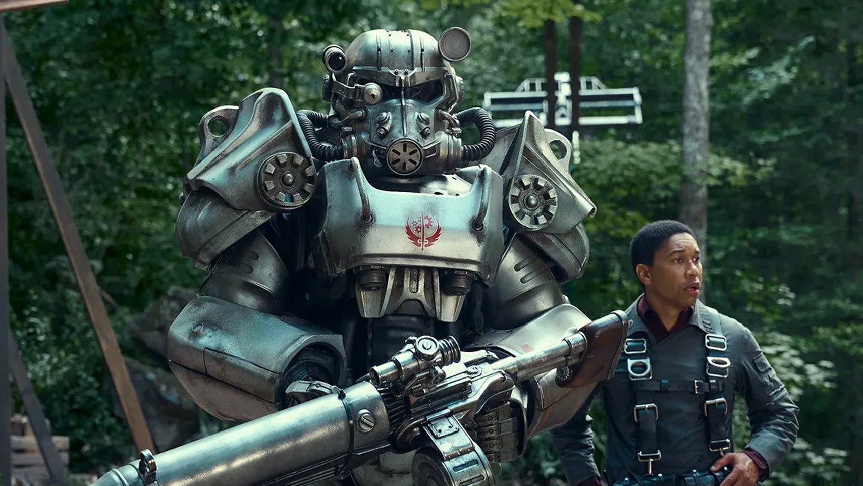 Maximus, a young man with a concerned look on his face, is stood behind someone wearing a full suit of power armour in the Fallout show. - 1