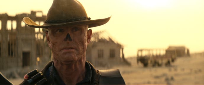 غول با بازی والتر گوگینز، در این صفحه از Fallout، با کلاه در مقابل شهری غروب آفتاب ایستاده است.