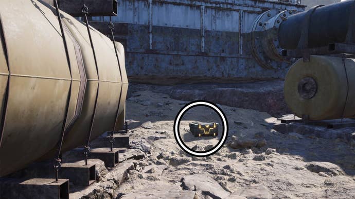 A circle highlights a reward chest sitting on the rocky ground between two large pipes.