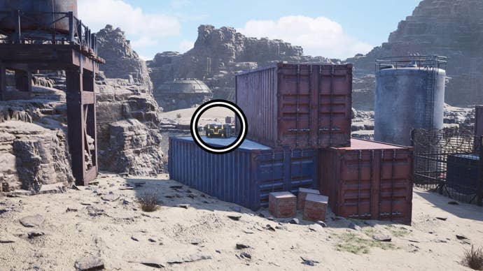A circle highlights a reward chest on a blue shipping container that’s beside two red shipping containers.