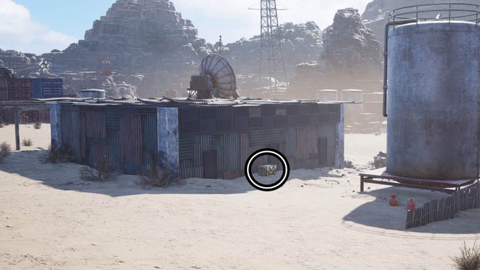 A circle highlights a reward chest on the ground beside a metal hut that has a large satellite dish on it.
