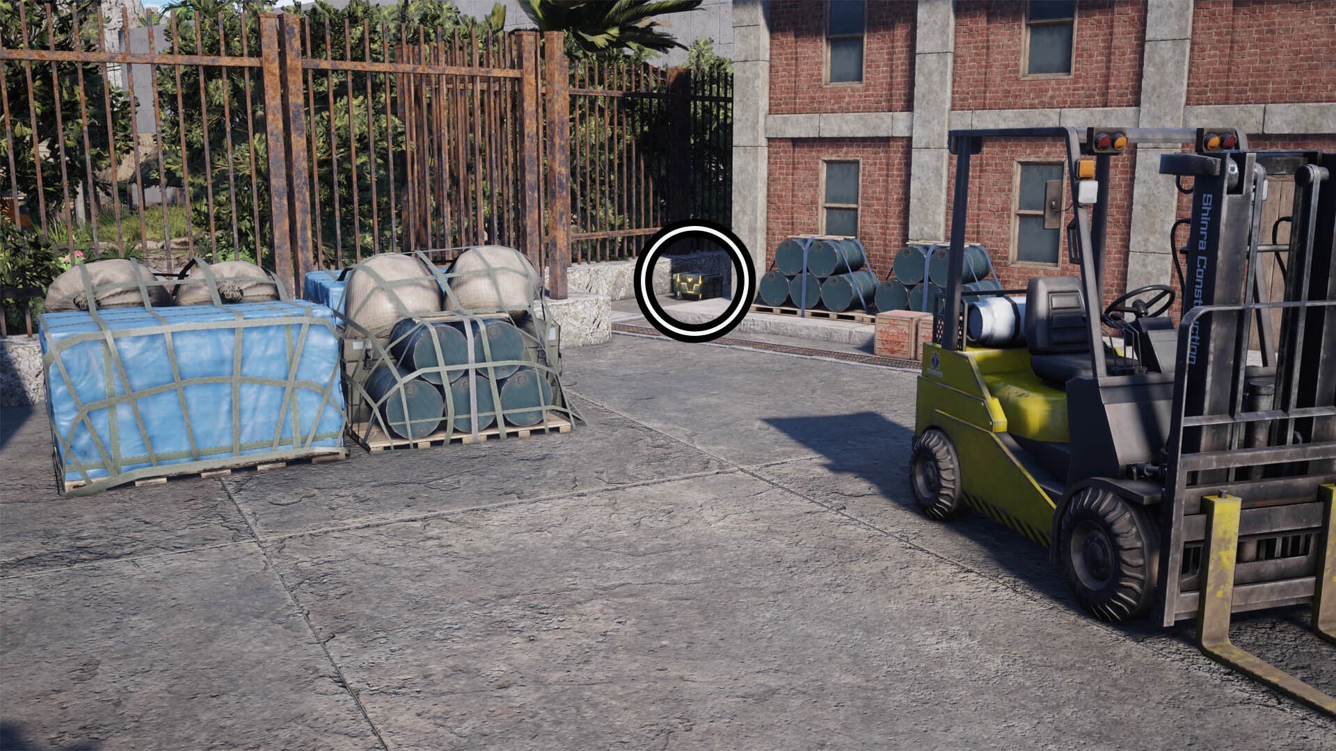 A circle highlights a reward chest beside a brick building in the distance, in the foreground is a yellow forklift truck on the right and some pallets on the left.