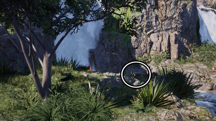 A circle highlights a reward chest sitting behind some foliage on the edge of an area close to a waterfall.