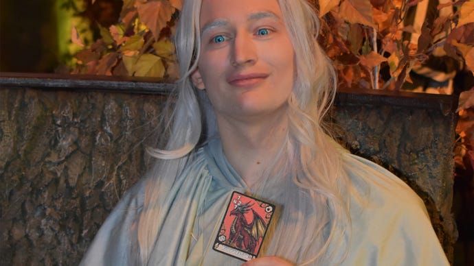 Sam, cosplaying as Venat from Final Fantasy XIV, holds up a Triple Triad card at Final Fantasy Fan Fest